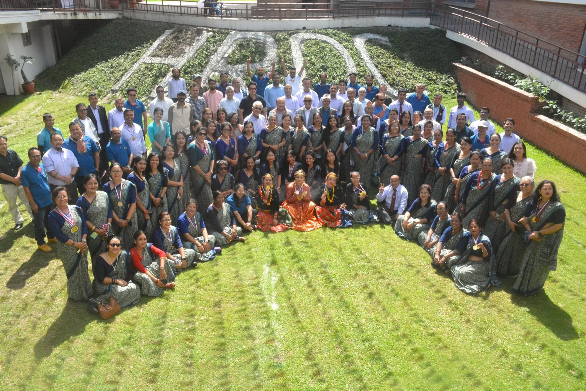 The HRDC staff: a large group of people gathered in a semicircle in four rows, looking up at an elevated camera