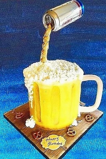 A realistically designed cake shaped like a beer mug with a beer can pouring a stream of liquid into it. The cake has a foamy top and is placed on a wooden board decorated with small pretzels. A "Happy Birthday" message is visible.