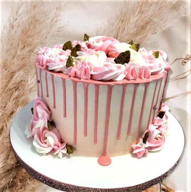 Elegant cake with pink and white frosting, decorated with floral designs and green leaves, featuring pink drip icing.