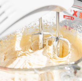 Close-up of a stand mixer with beaters mixing yellow cake batter in a glass bowl.