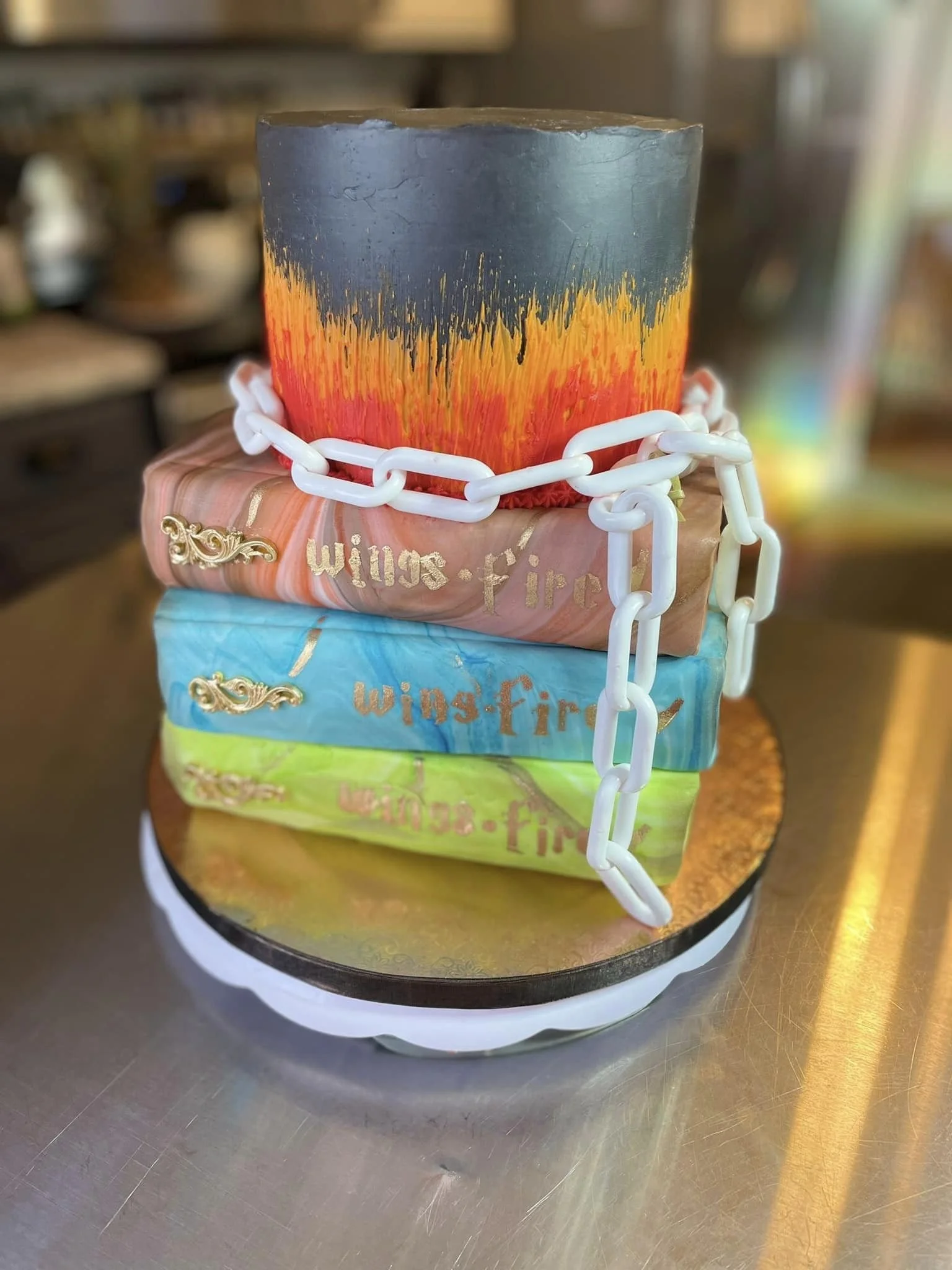 A cake designed to resemble a stack of books with a fiery-themed top layer and chain decoration.