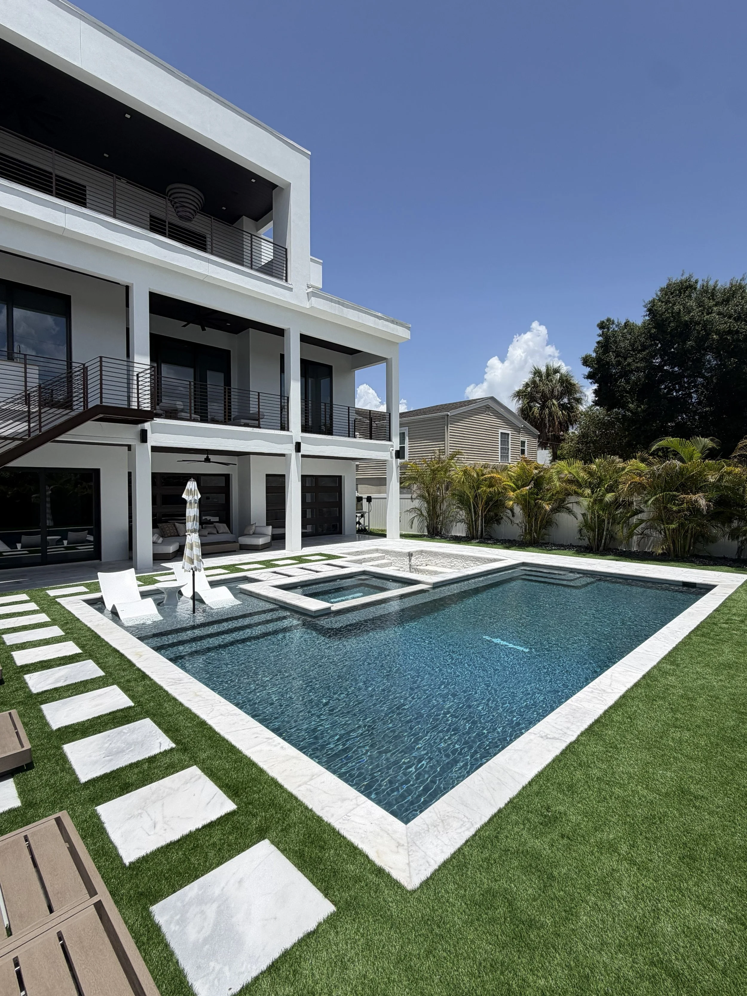 A modern house with a black swimming pool and a patio area surrounded by green grass and potted plants.