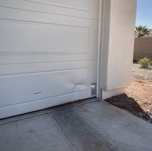 White garage door with rust stains on concrete driveway next to stucco house wall and desert landscaping.