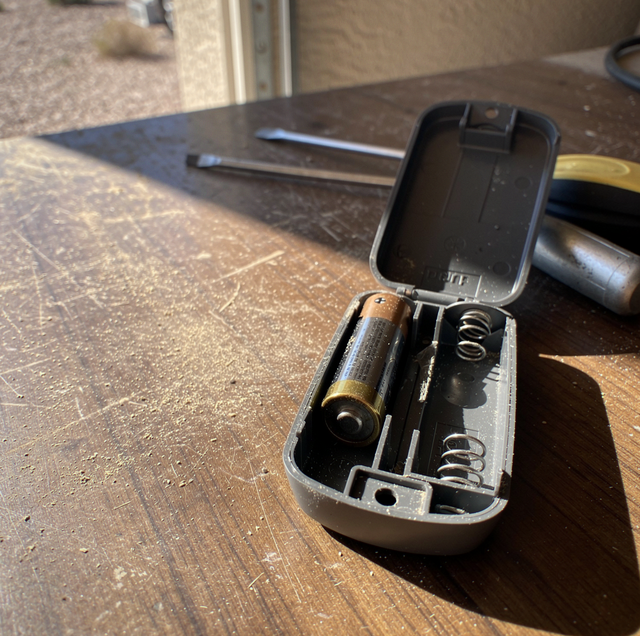 An open battery compartment with an AA battery and metal springs inside sits on a wooden table.