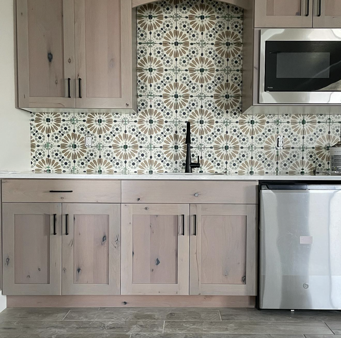 Kitchen with light wood cabinets, patterned tile backsplash, black faucet, microwave above, and a small fridge below the counter.