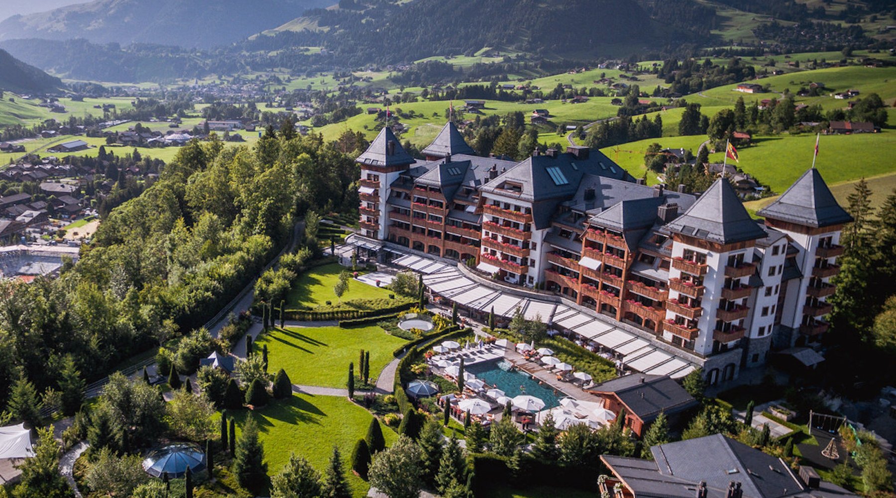 Aerial view of a large luxury hotel with towers and landscaped gardens, surrounded by lush green hills.