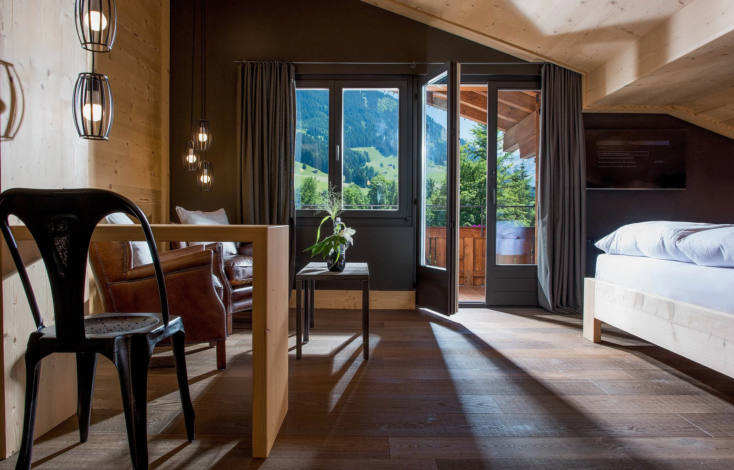Modern bedroom interior with wooden furniture, large windows showing a scenic mountain view, and hanging lights on the left.