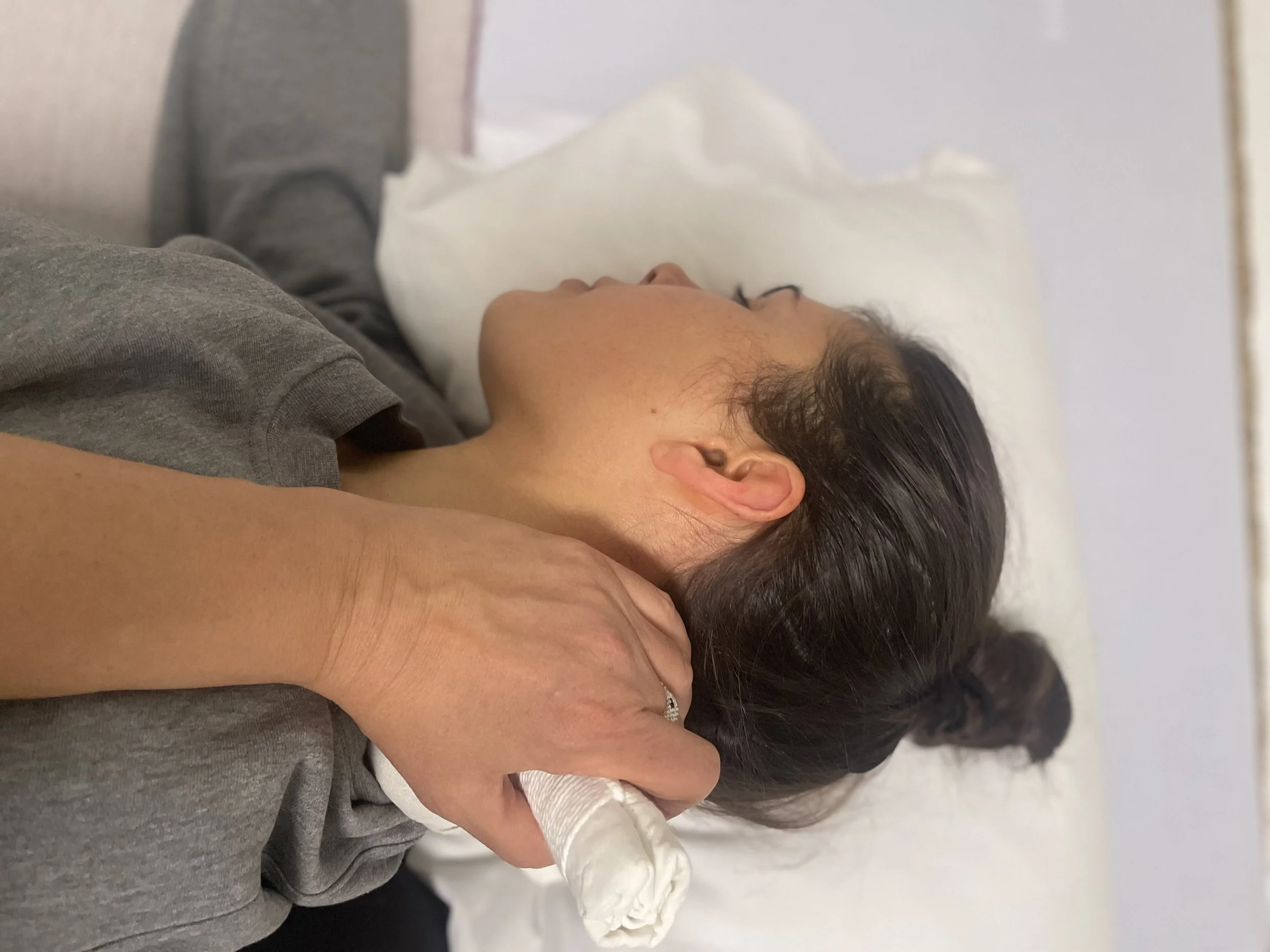 A woman lying on her side on a bed, receiving a neck massage from another person.