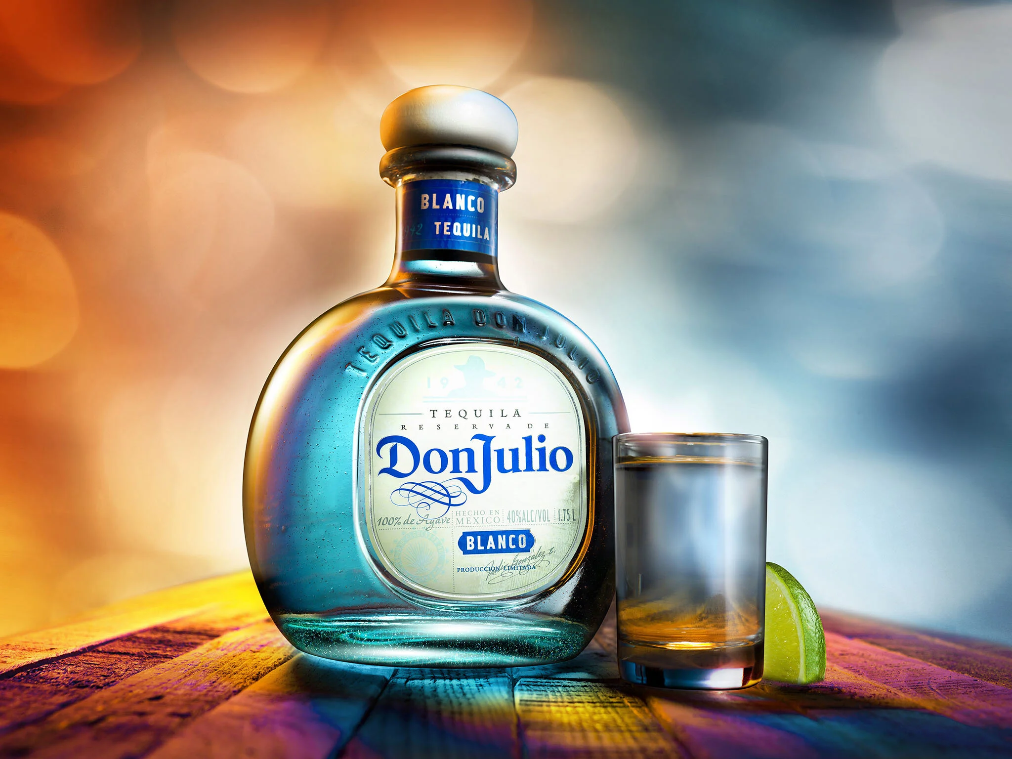 Don Julio Blanco tequila bottle with shot glass and lime wedge on colorful wooden table.