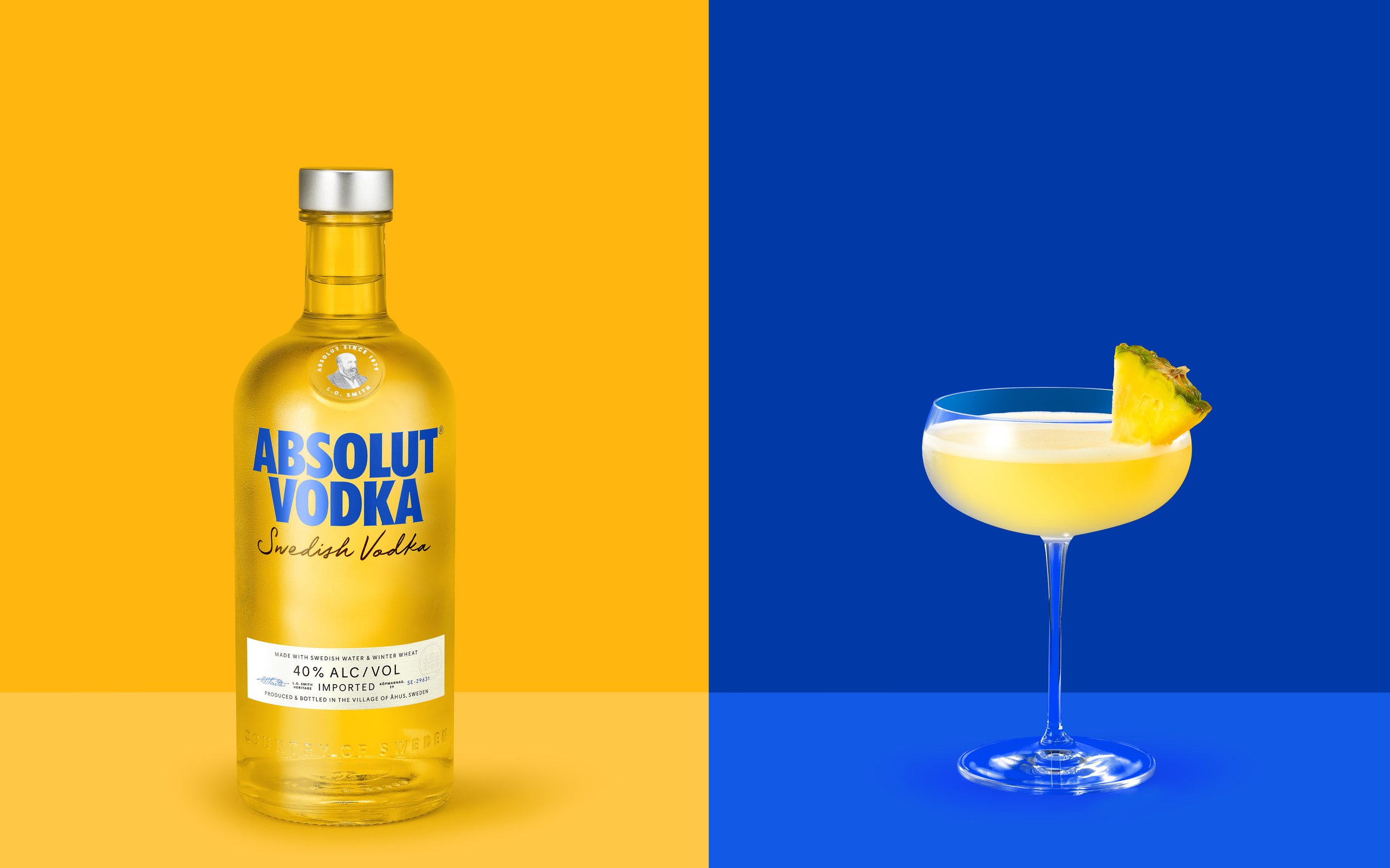 Absolut Vodka bottle and pineapple cocktail on colorful background.