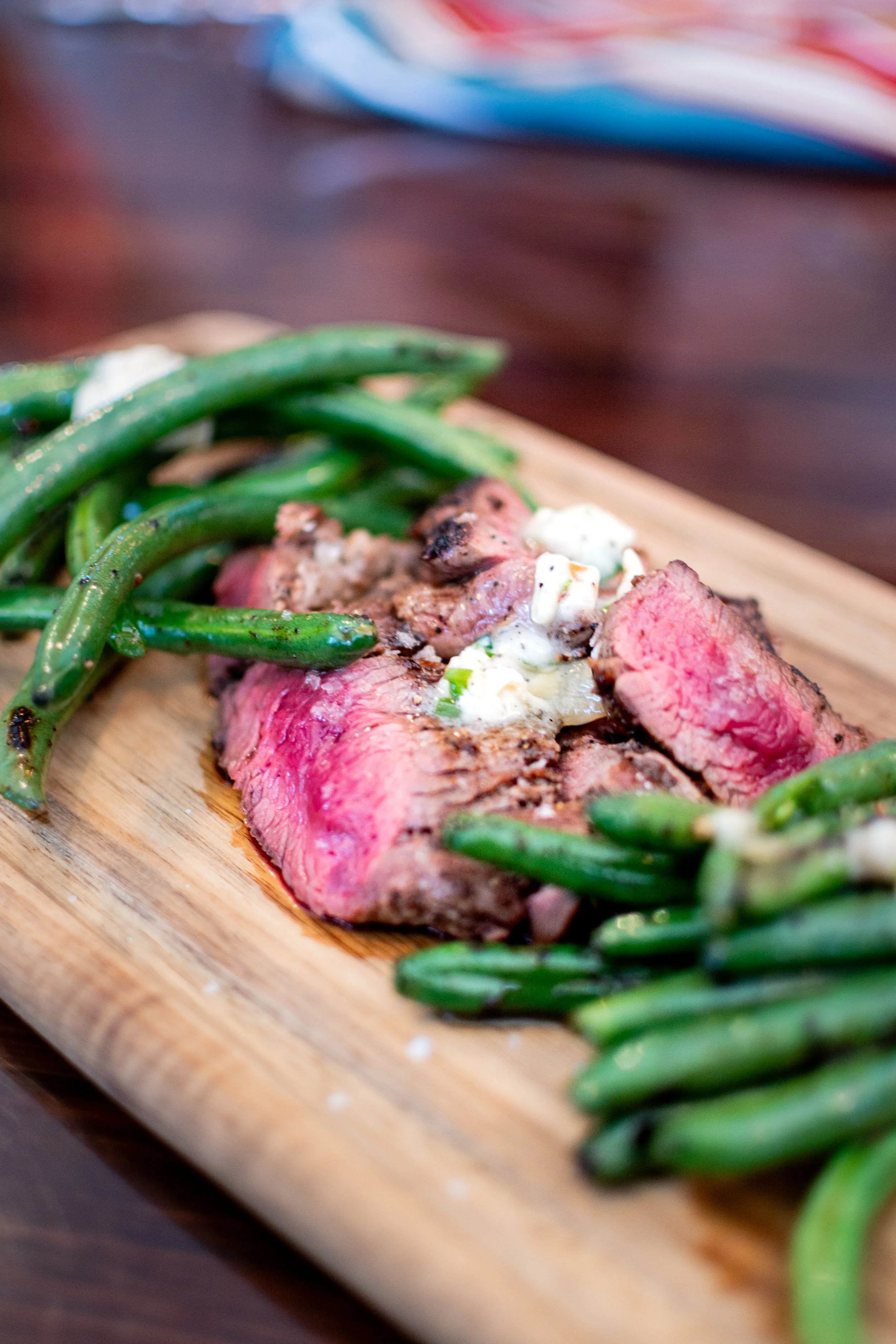 A close-up of a plated meal with slices of cooked steak topped with a creamy sauce, served with green beans on a wooden cutting board.