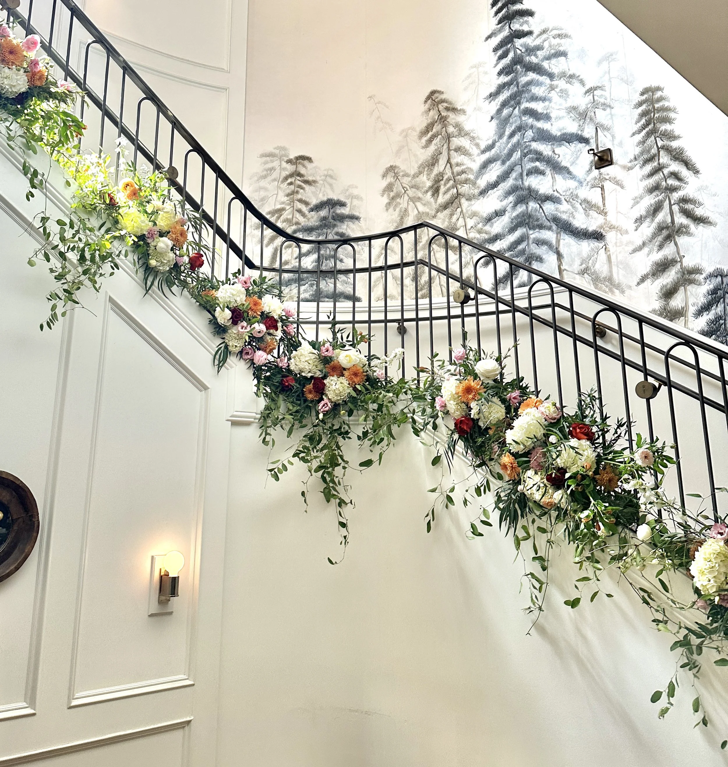 Wedding floral installation on an interior staircase with black metal railing, decorated with an arrangement of colorful flowers including white, pink, red, and orange blooms. Created by Boise wedding florist at Edwards Flowershop.