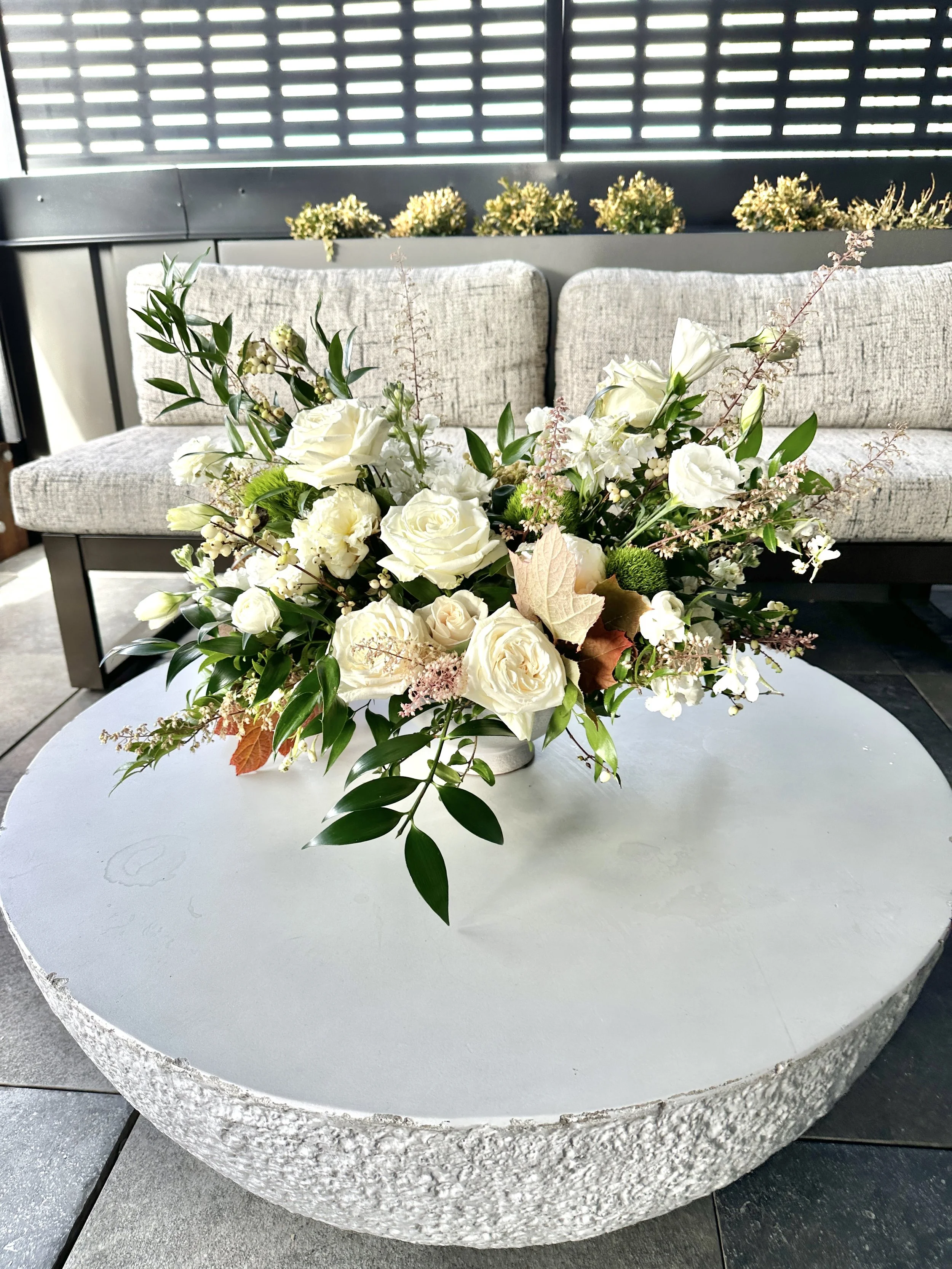 A wedding bouquet of white roses and various greenery on a white round table with a textured edge. Created by Boise wedding florist at Edwards Flowershop.