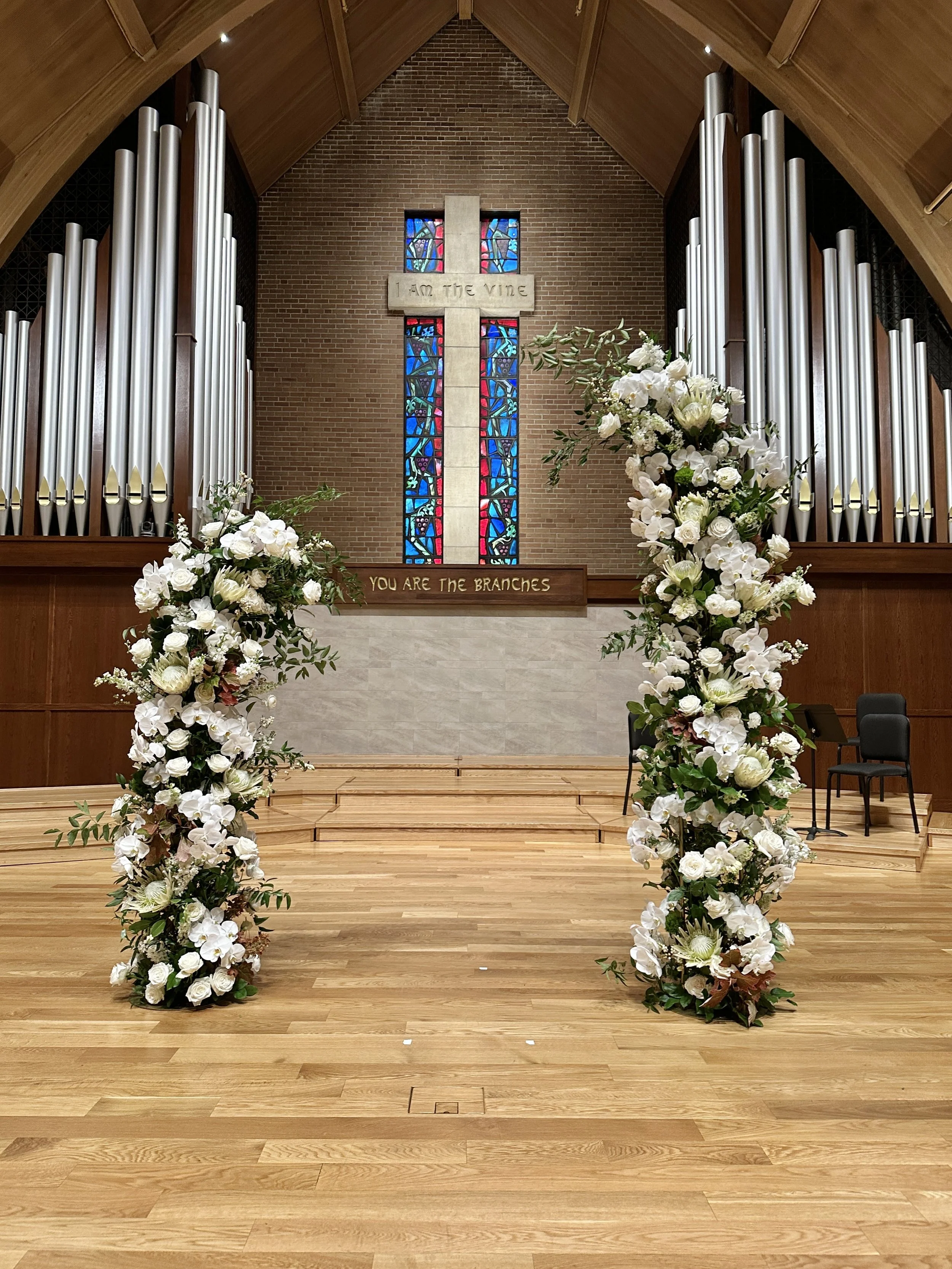 A large floral archway for a church wedding ceremony, created by Boise wedding florist at Edwards Flowershop, featuring white flowers and lush greenery.