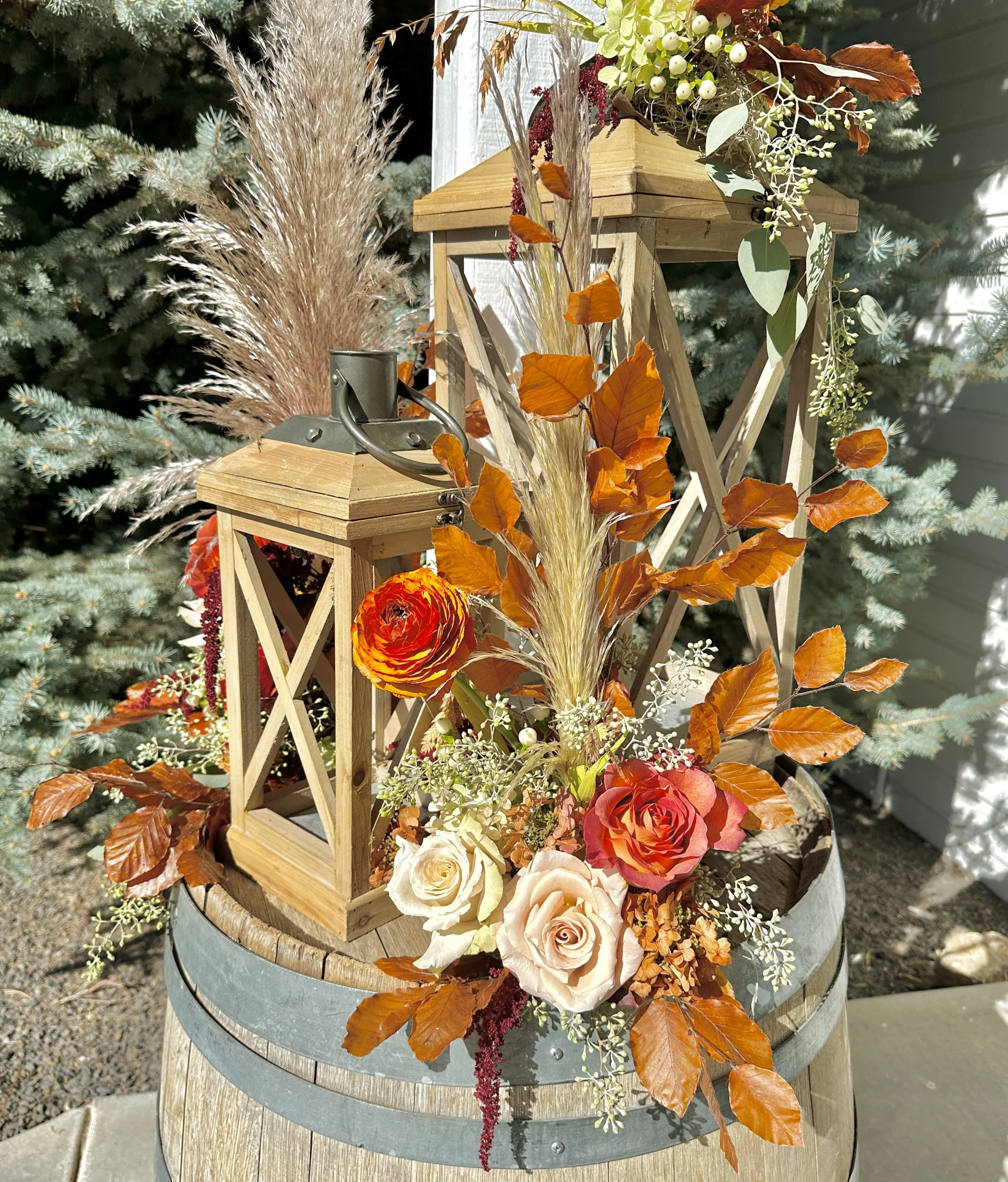 Decorative floral arrangement for an Autumn wedding with orange, cream, and white roses, dried grass, and green and brown leaves on a wooden and metal stand. Wedding flowers by Boise florist Edwards Flowershop.