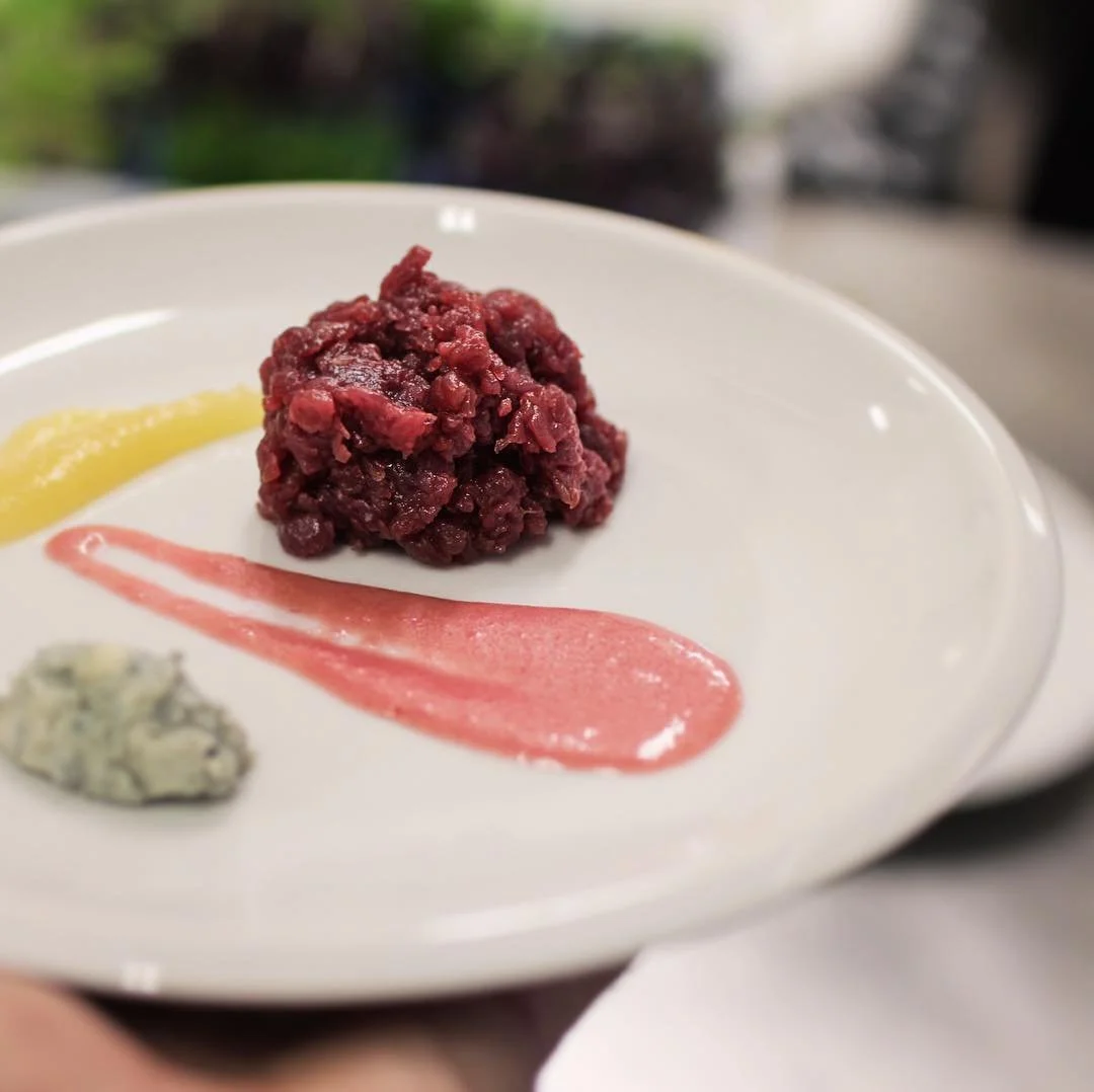 Raw steak tartare on a white plate, garnished with yellow, red, and green sauces