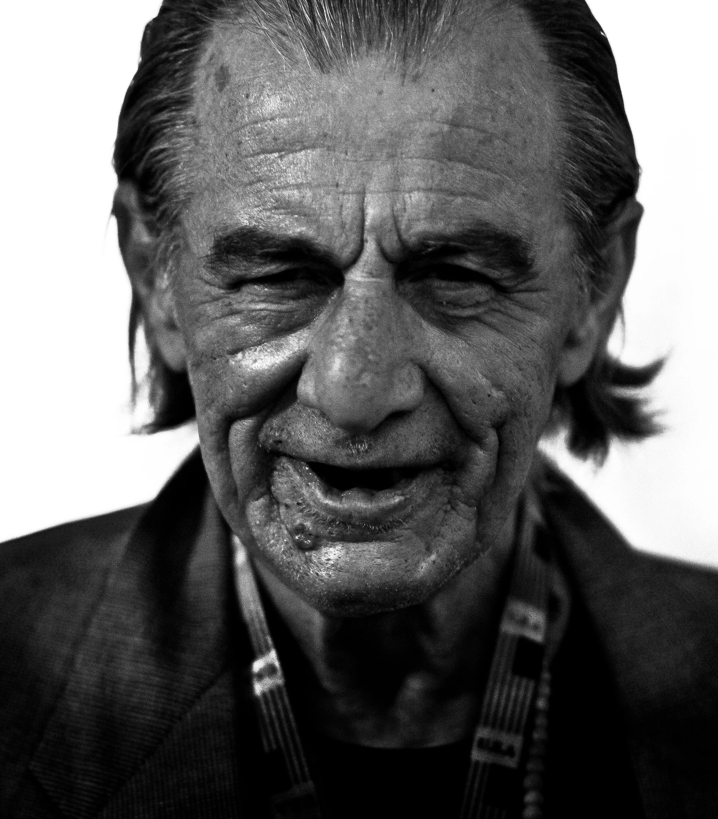 Close-up of a smiling elderly man with gray hair, wearing a checkered shirt, in black and white.