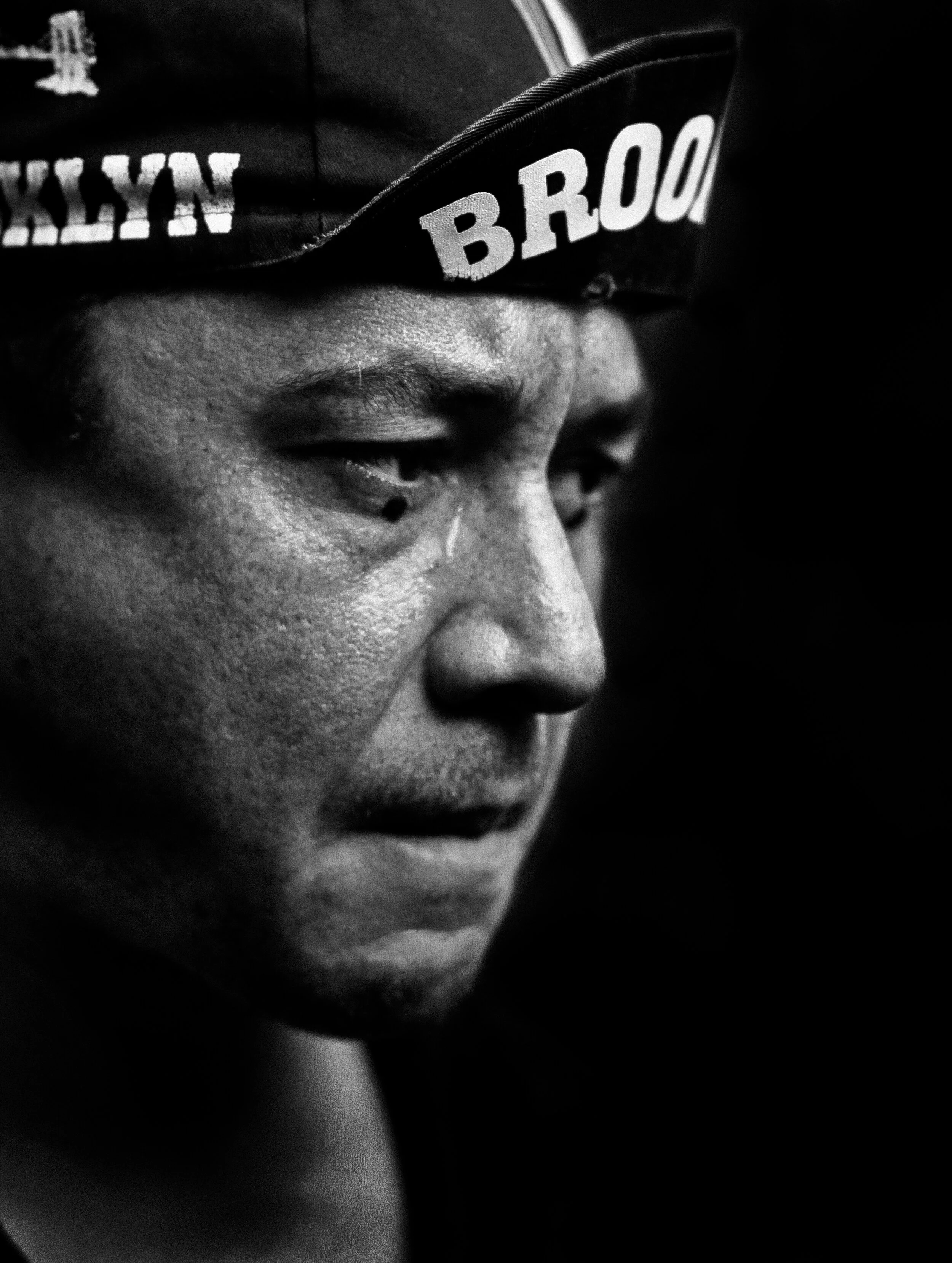 Close-up of a person wearing a cap with the logo 'BRO' on it, in black and white.