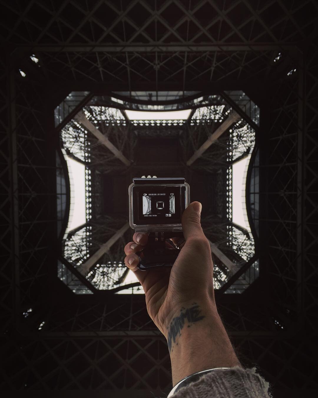 Looking up at the Eiffel Tower from underneath with a person holding a camera, capturing the view.