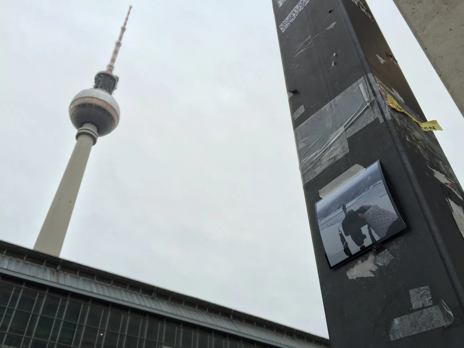 View of the Berlin TV Tower in Berlin, Germany, with a black electronic device and a photo of a person on a beach in the foreground.