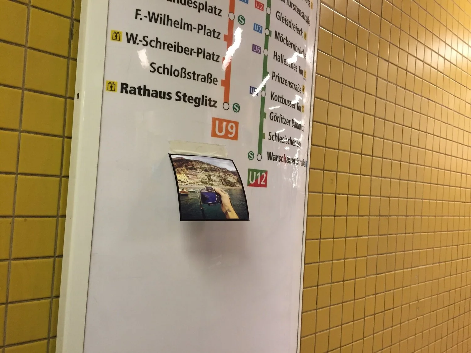 Berlin subway map on yellow tiled wall with a photo of a hand holding a smartphone in front of a cityscape.