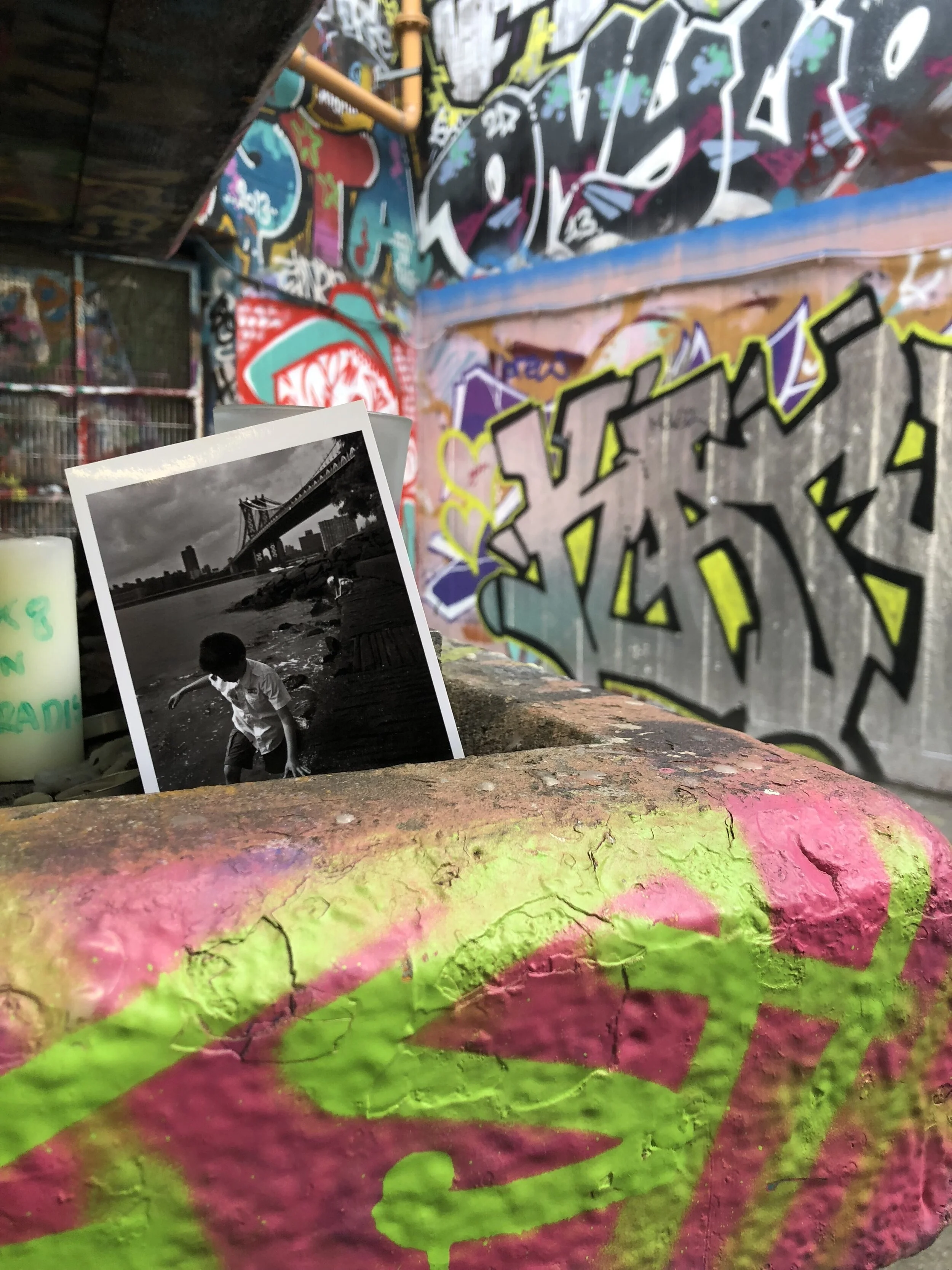 Colorful graffiti on a concrete wall in an urban setting, with a black and white photograph of a boy playing near a bridge placed in front of the wall.