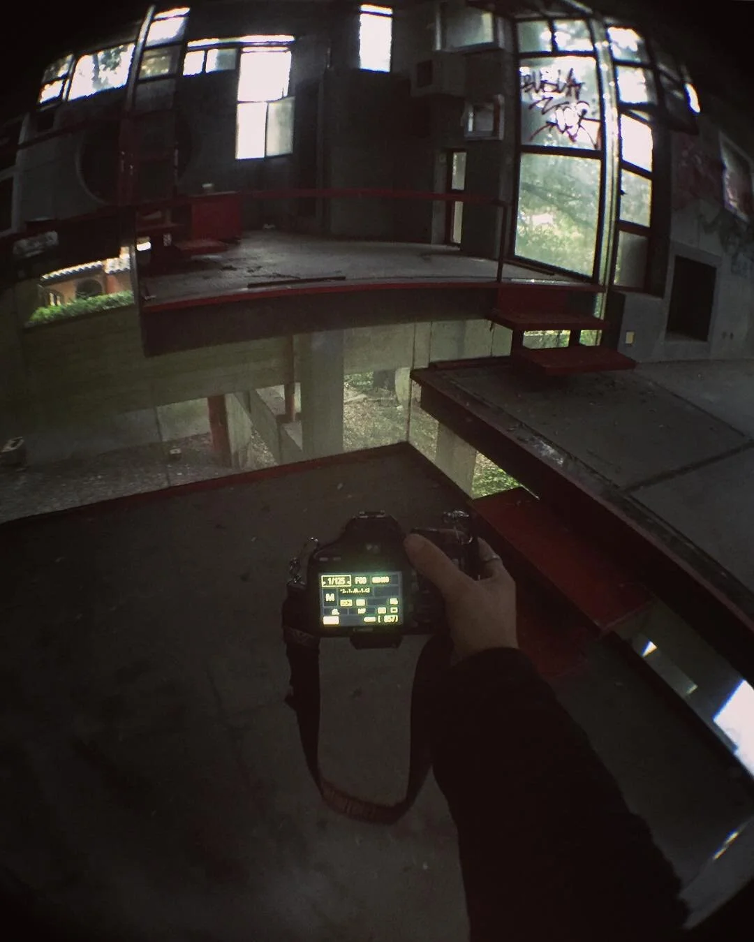 Photo of an abandoned building's interior with broken windows, graffiti on the walls, and a person holding a camera.