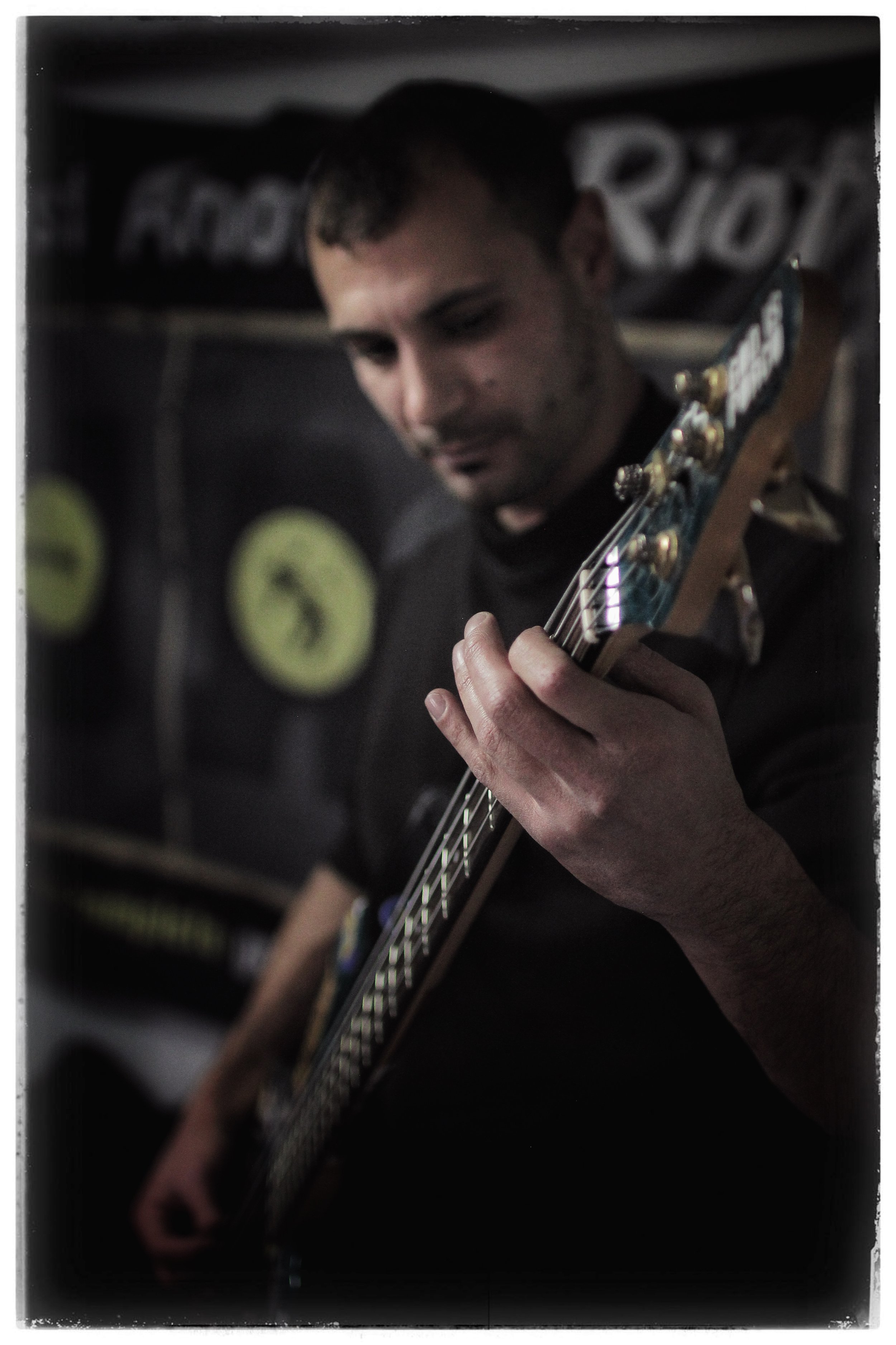 A man playing an electric guitar, focused on the fretboard, with amplifier and guitar pedals in the background.