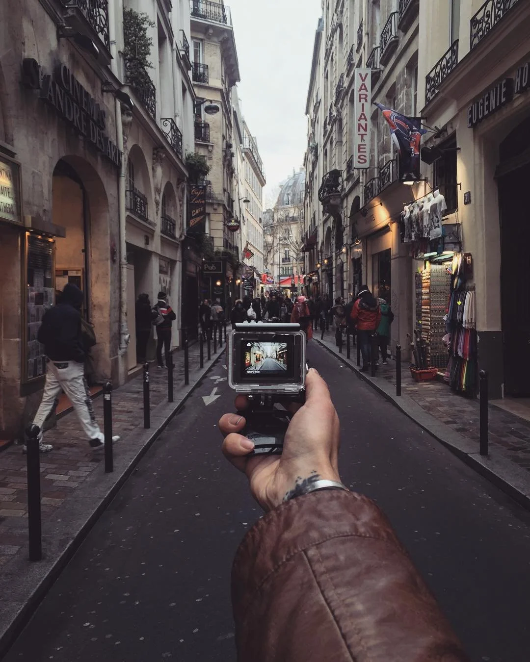 Person holding a camera taking a picture of a city street with shops and pedestrians, historic buildings on either side.