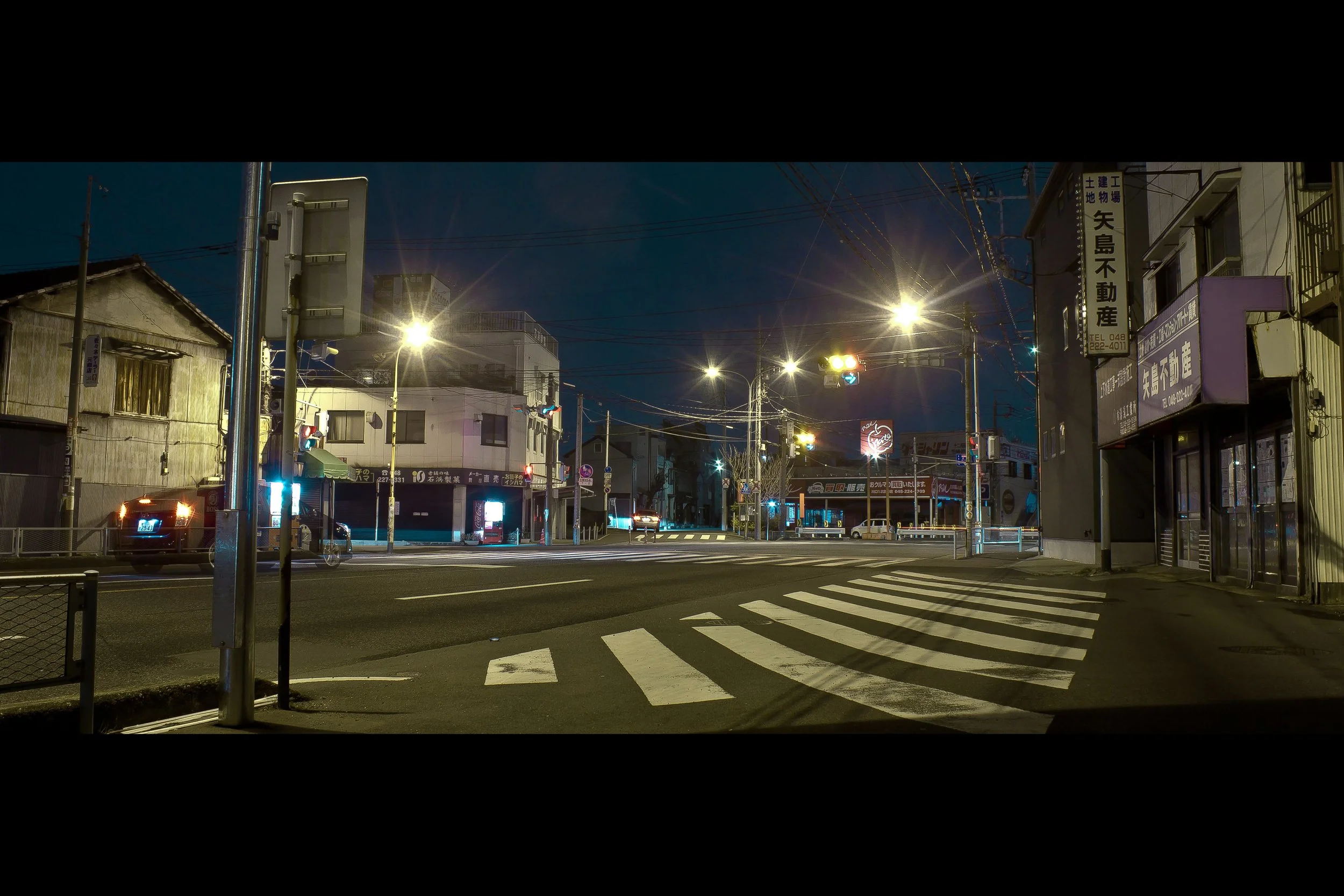 Nighttime view of a city street with traffic lights, buildings, and streetlights illuminating the scene.