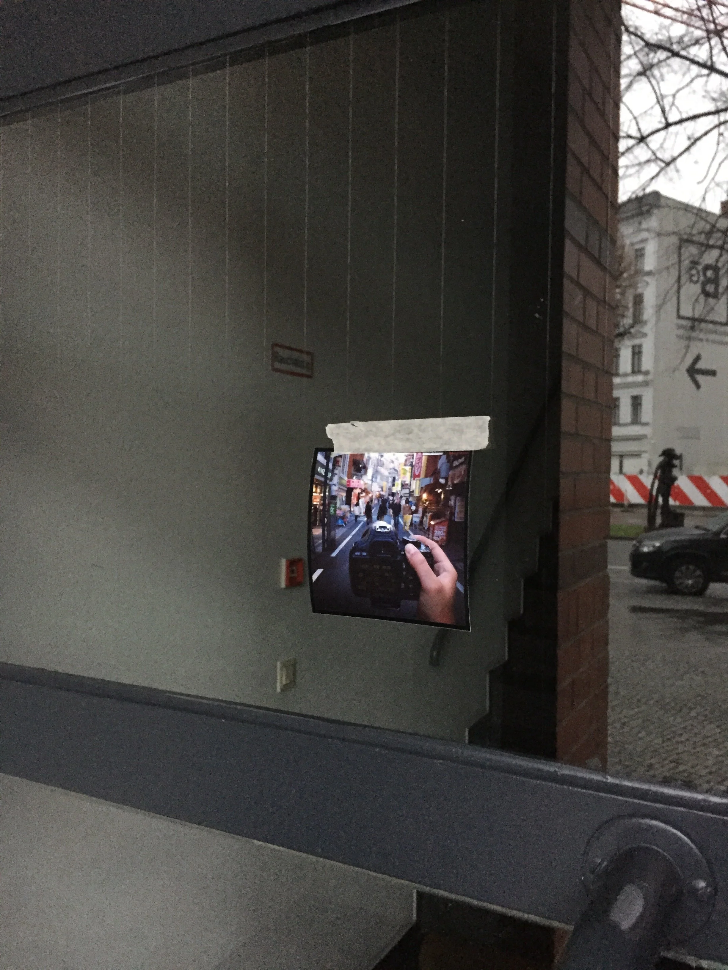 A mirror on a wall reflects a TV screen showing a person holding a phone taking a picture, with a street scene including cars and buildings visible outside.