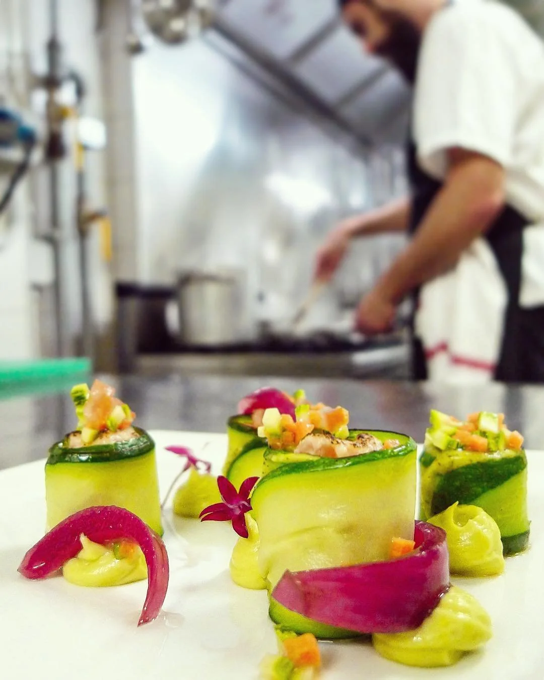 Vegetable or seafood roll appetizers garnished with colorful vegetables and edible flowers, set on a white plate in a professional kitchen.
