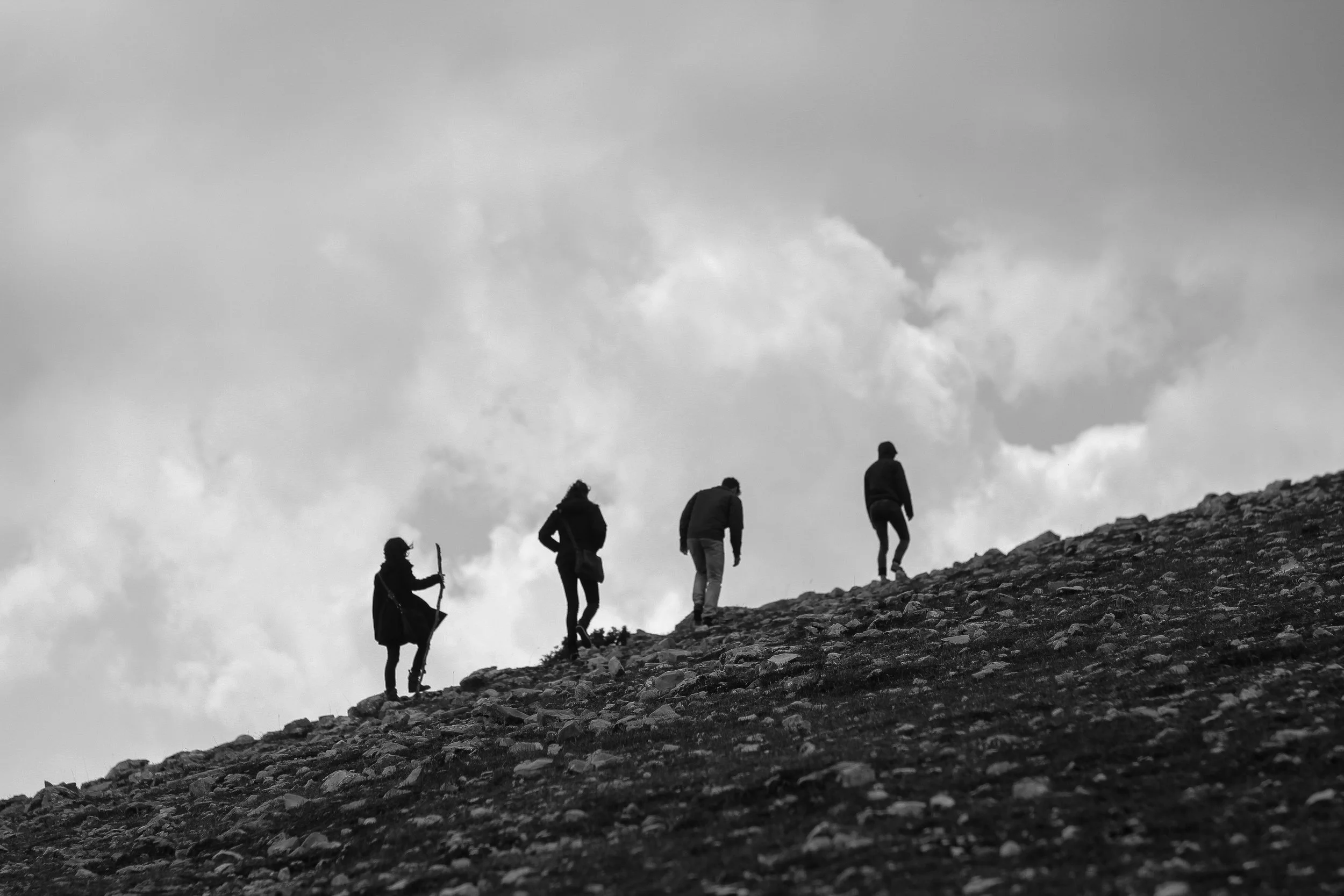 A small group of people hiking up a rocky hillside against a cloudy sky.