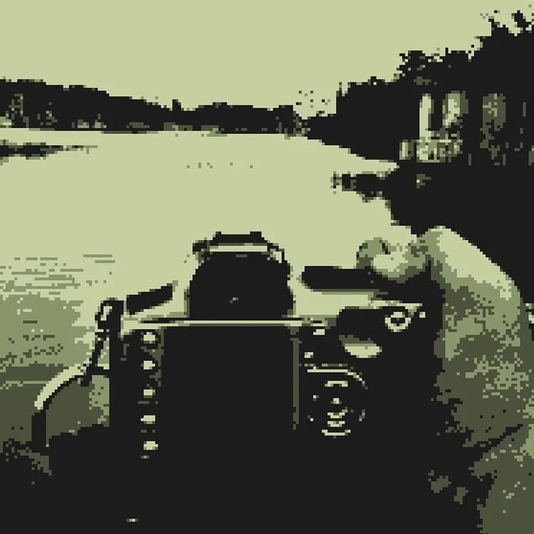 A person holding a camera while kayaking or canoeing on a river surrounded by trees.