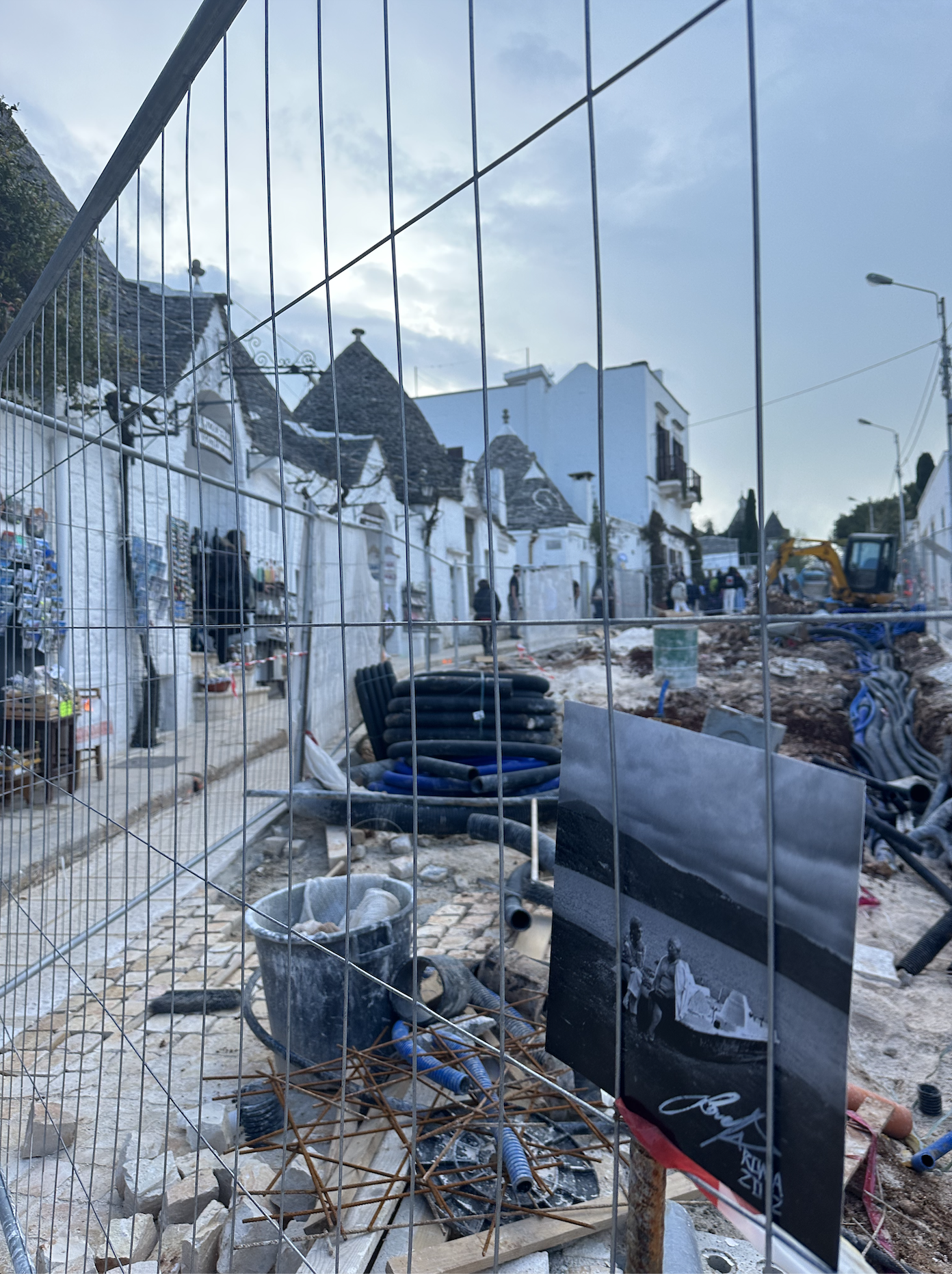 Construction site with scaffolding, pipes, and workers in the background, enclosed by a metal fence.