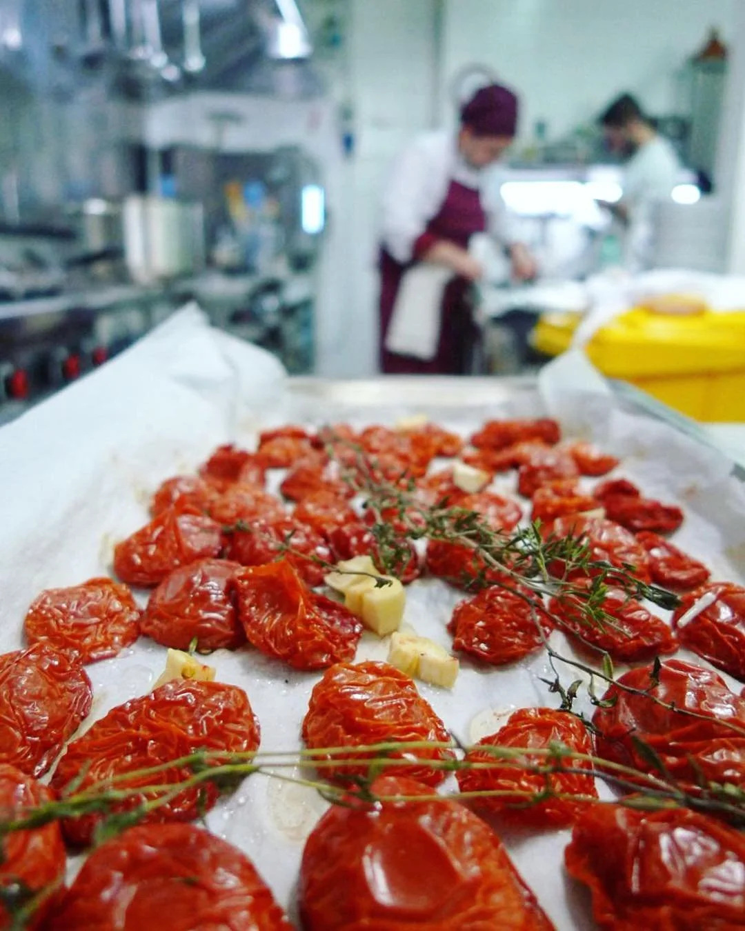 Freshly prepared sun-dried tomatoes garnished with a sprig of thyme and small chunks of cheese on a tray in a professional kitchen.