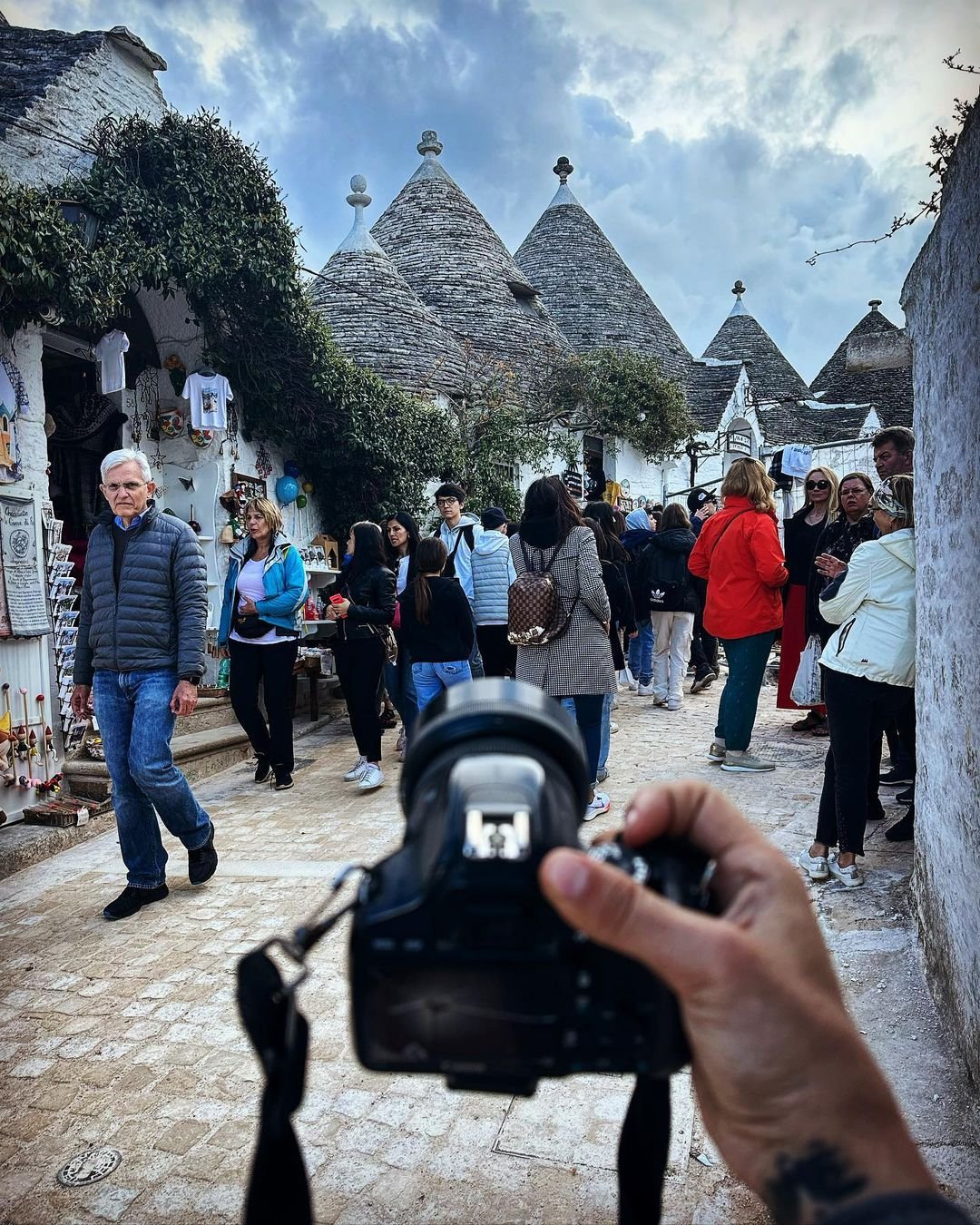 A street scene in a historic town with tourists and the iconic cone-shaped roofs of trulli houses in the background.