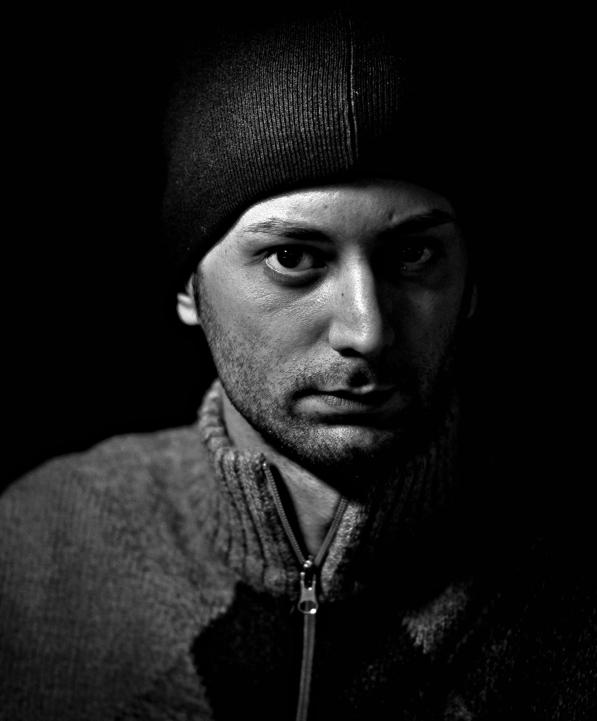 Close-up of a person's face, focusing on the eyes, wearing a dark beanie and a zipped sweater, in black and white.