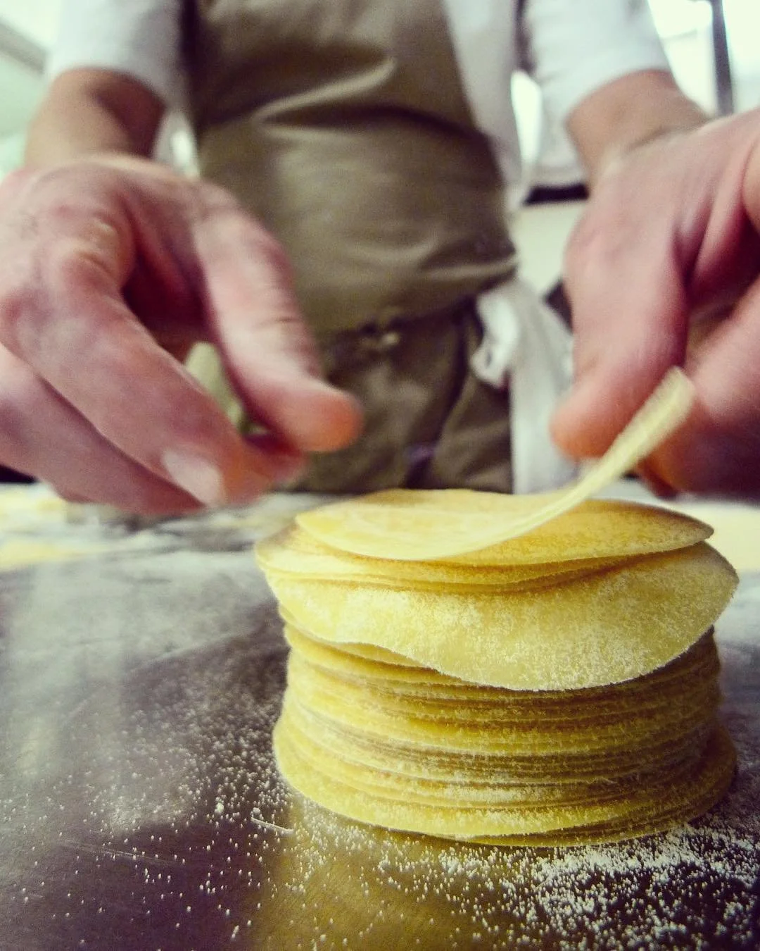 Close-up of a person stacking thin, round potato chips on a surface dusted with flour.