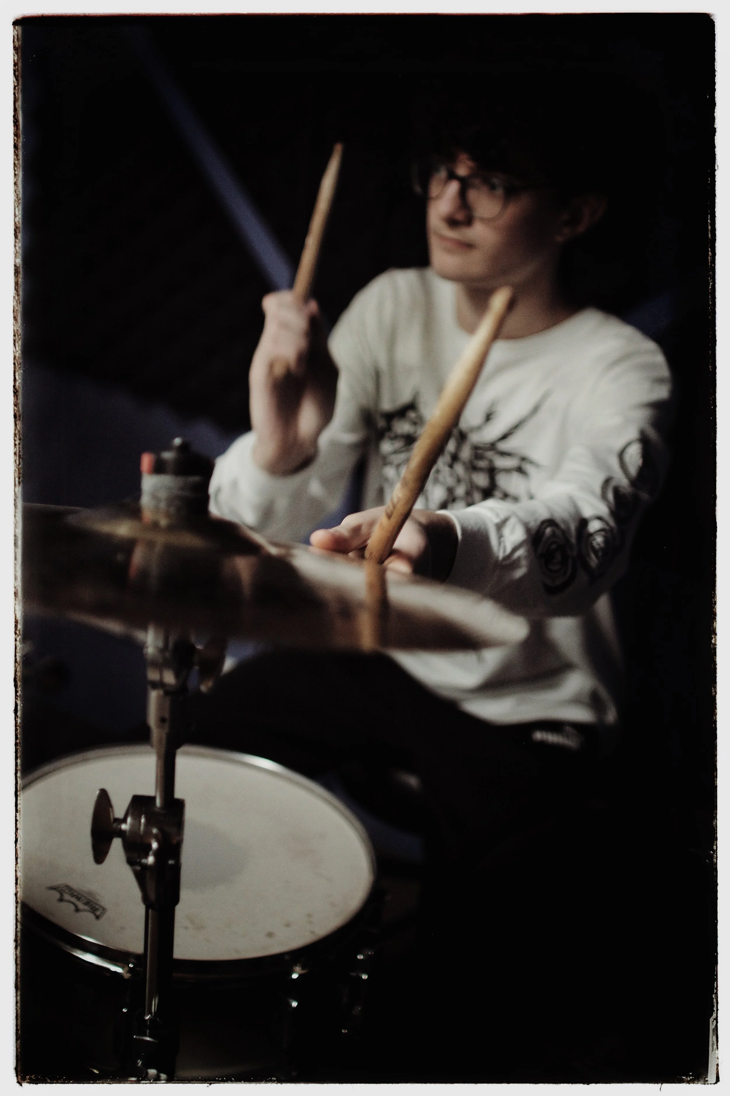 A person with glasses playing a drum set in a dark room.