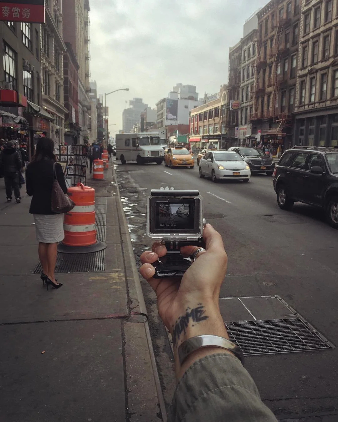Person holding a camera takes a picture of a city street with cars and buildings.