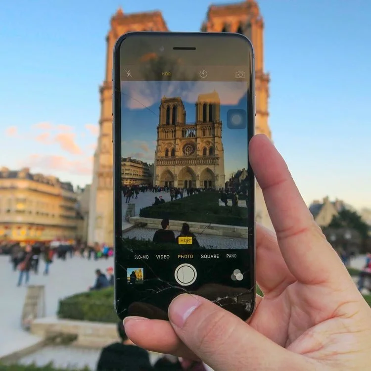 A person taking a photo of Notre-Dame Cathedral in Paris with a smartphone.