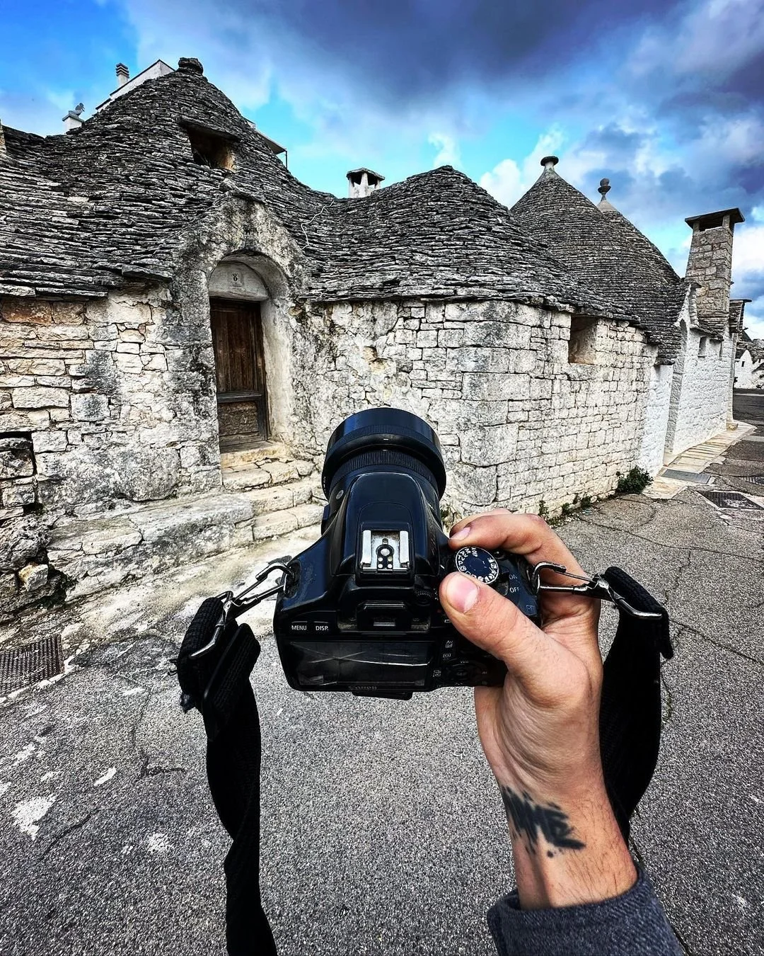 Person holding a camera filming traditional stone houses with conical roofs in a village.