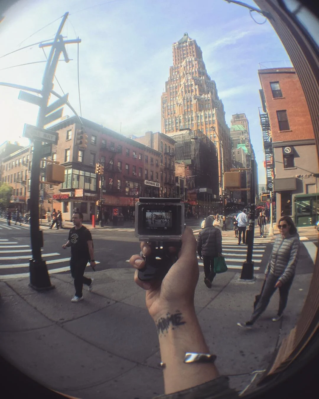 City street scene with pedestrians, tall buildings, and a reflecting fisheye view of the person taking the photo with a handheld camera.
