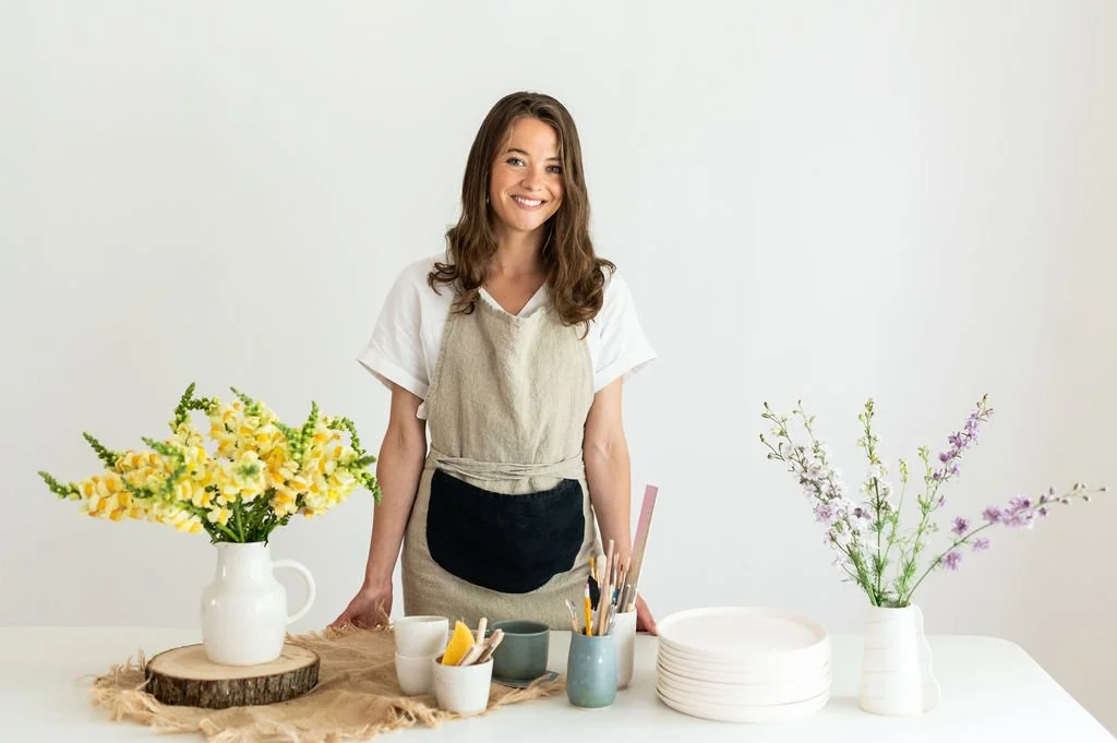 Illinois Local member and ceramic artist smiling behind a table of handmade pottery, plates, and fresh flowers