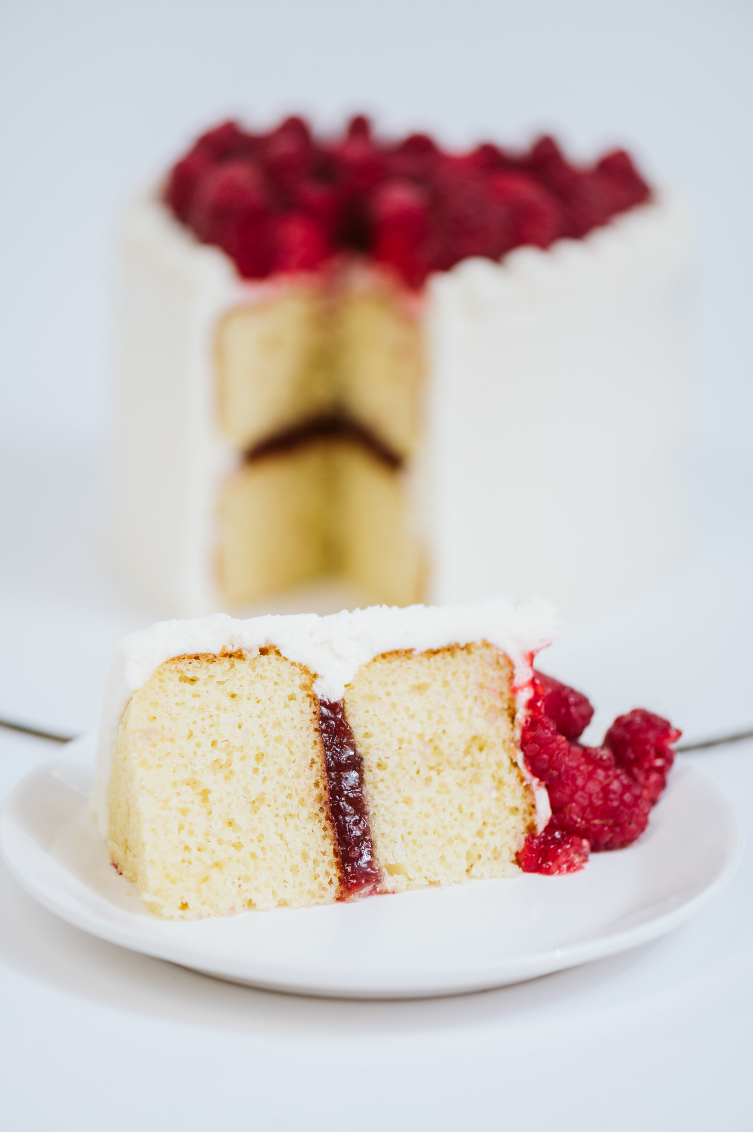 A white heart shaped cake with fresh raspberries