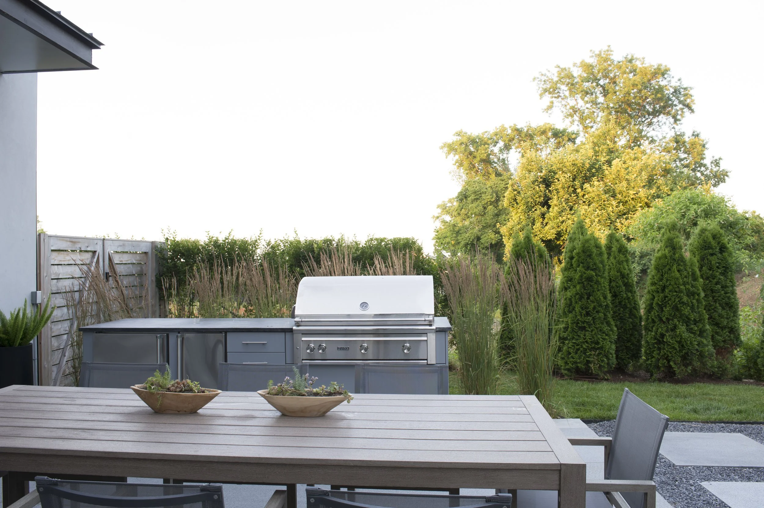Outdoor kitchen with a built-in grill, backed by tall ornamental grasses
