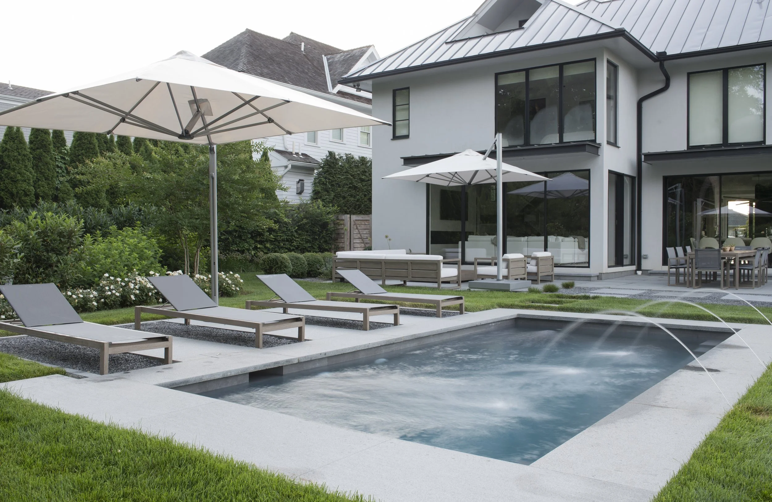 Pool terrace with chaise lounges and white umbrellas beside a modern white house