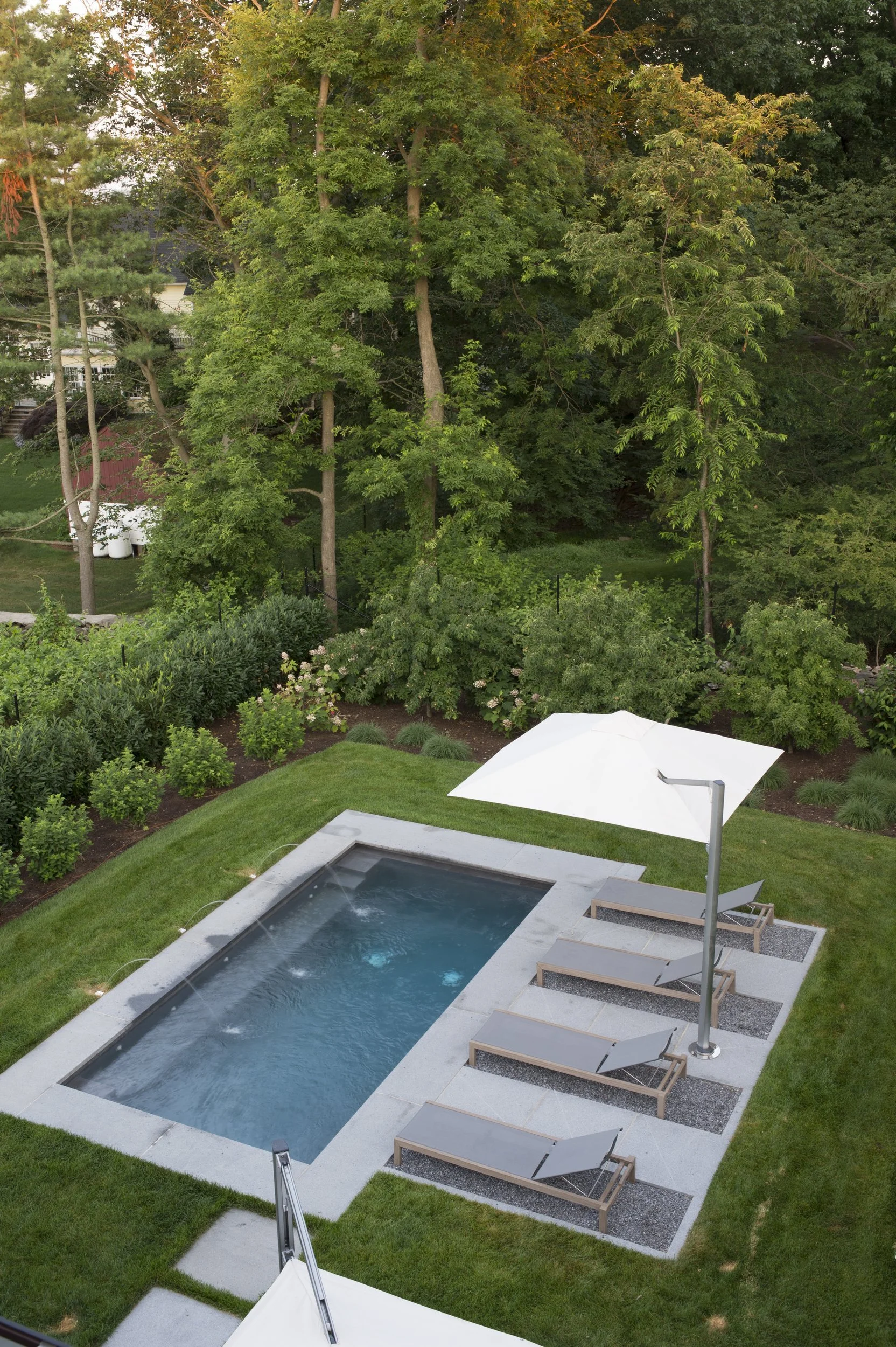 View from above of a rectangular pool set in lawn, with chaises and a white umbrella