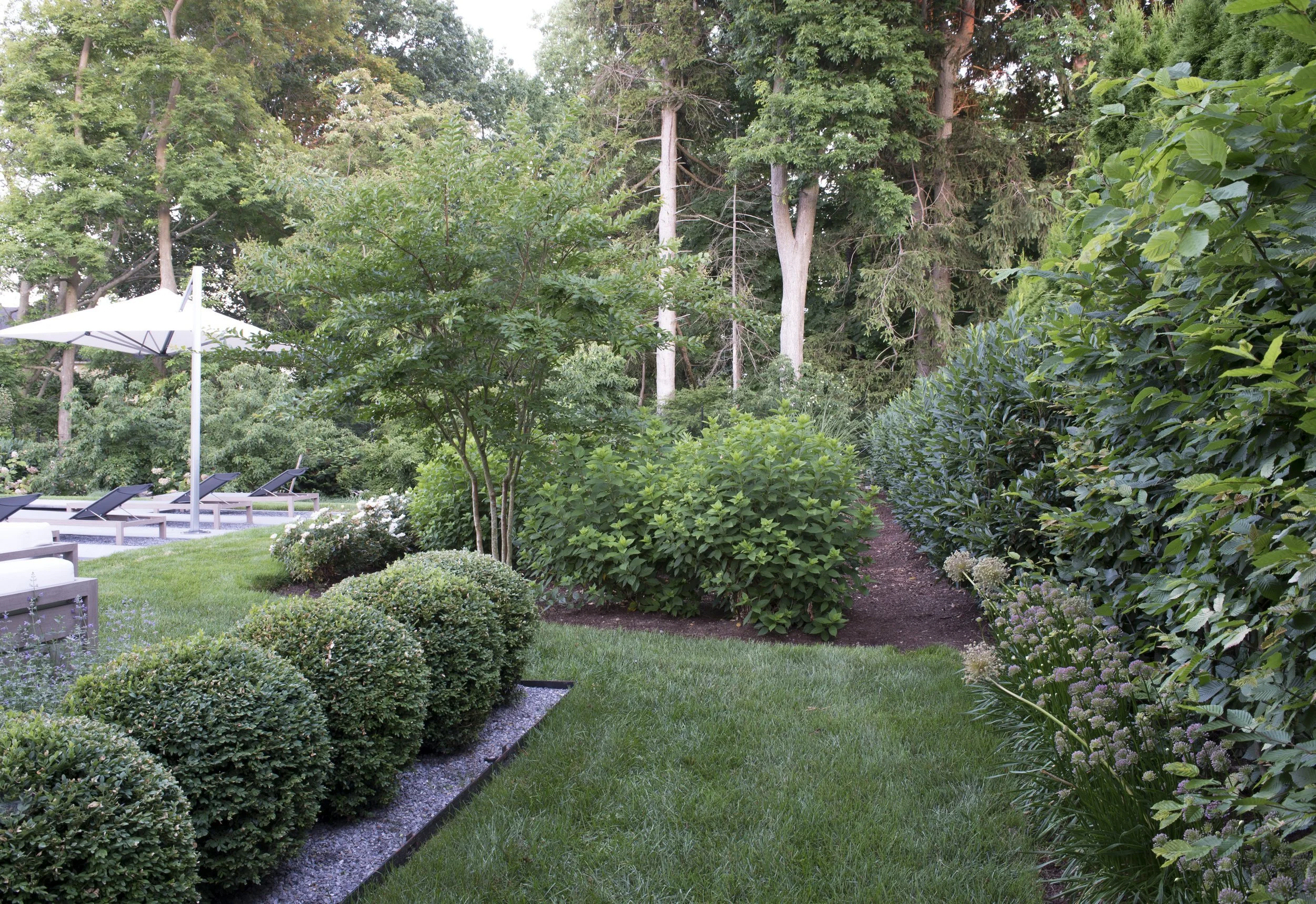 Clipped boxwood spheres and flowering shrubs along a stone-edged lawn